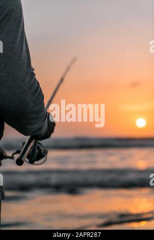 Uomo pesca sulla spiaggia al tramonto Foto Stock