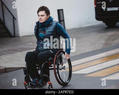 Mosca, Russia - 17 gennaio 2020: Un uomo siede su una sedia a rotelle su ruote mentre guida attraverso la strada sul crocevia zebra Foto Stock