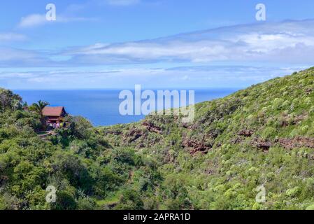 Una piccola casa solitario si trova sulle scogliere tra la foresta verde e sopra lo scintillante e blu Oceano Atlantico. La lavanderia colorata asciuga nel sole estivo Foto Stock