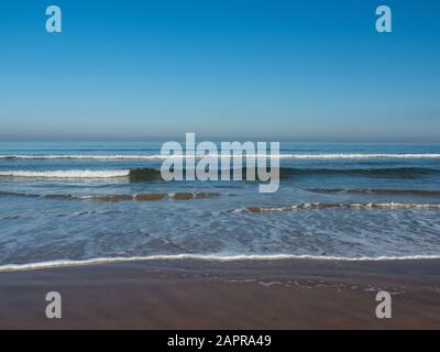 Onde dolci rotolano in spiaggia in una giornata di sole, con un cielo blu perfetto e vista dell'orizzonte sgargiante. Saltburn-by-the-Sea, North Yorkshire - Regno Unito Foto Stock