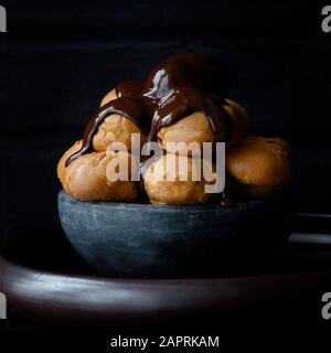 Profiteroles , scuri e succhietti ricoperti in una ricca salsa al cioccolato Foto Stock