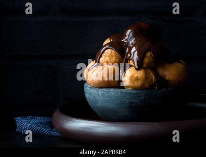 Profiteroles , pasta choux ricoperta in una salsa di cioccolato ricco di colore scuro Foto Stock