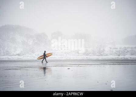 Surfista che cammina lungo la spiaggia nel Maine durante una tempesta di neve d'inverno Foto Stock