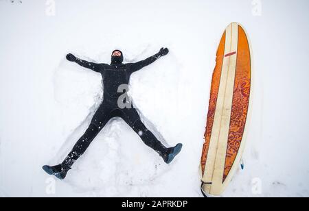 Il surfista fa l'angelo della neve nella tempesta invernale della neve del Maine Foto Stock