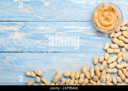 Pasta di arachidi cremosa in vaso di vetro aperto e arachidi nel guscio. Pasta di arachidi cremosa piatto con posto per testo su sfondo blu legno per la cottura Foto Stock