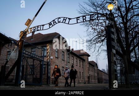 24 gennaio 2020, Polonia, Oswiecim: Nel tardo pomeriggio, i visitatori camminano attraverso la porta dell'ex campo di concentramento di Auschwitz i con l'iscrizione 'Arbeit macht frei'. 27.01.2020 ricorre il 75th anniversario della liberazione del campo di concentramento da parte dell'Armata Rossa. Dal 1940 al 1945, la SS gestiva il complesso con numerosi campi satellite come campi di concentramento e di sterminio. Il numero di coloro che sono stati uccisi ammonta a 1,1 - 1,5 milioni, la maggior parte dei quali ebrei. Auschwitz è il simbolo dell'omicidio di massa industriale e dello sterminio degli ebrei. Foto: Kay Nietfeld/Dpa Foto Stock