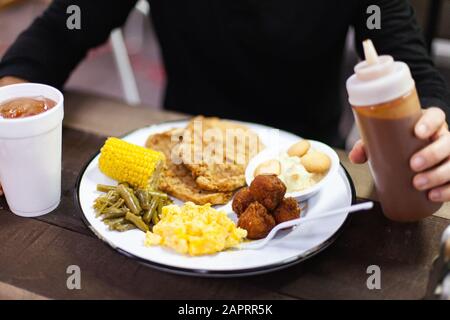 Un uomo tiene una bottiglia di salsa barbecue su un piatto di cibo ad un buffet Foto Stock