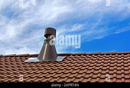 Tubo camino da acciaio inossidabile sul tetto della piastrella. Camino contro cielo blu. Foto Stock