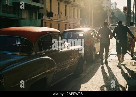 Havana, CUBA - 10 dicembre 2019: Un marciapiede con le persone che camminano vicino alle auto durante il giorno girato da dietro Foto Stock