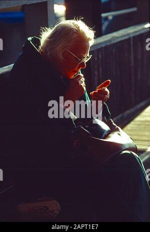 Donna anziana seduta all'aperto su una panchina della città. Foto Stock