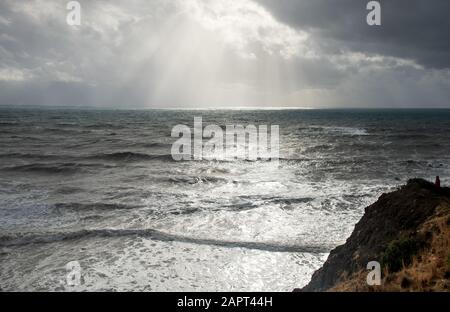 Persona non riconosciuta che si trova sul bordo di una scogliera che si gode il mare drammatico tempestoso. Roccia di Aphrodite costa a Cipro di Paphos Foto Stock