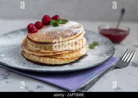 Una pila di deliziose frittelle con lamponi, more e mirtilli. Su uno sfondo chiaro. Cosparso di zucchero a velo e decorato con min Foto Stock