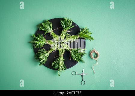 Fasci di rucola freschi su una piastra rotonda nera su un tavolo verde. Sopra la vista delle piante di rucola. Fare fasci da rucola. Rucola appena raccolta Foto Stock