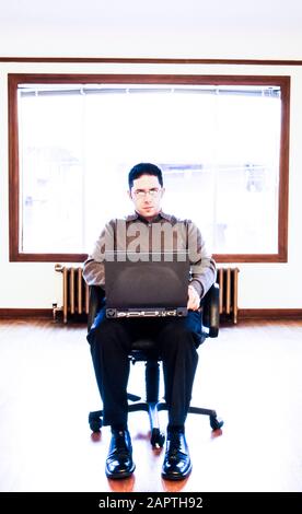 Ritratto di un uomo d'affari in una stanza vuota con un computer portatile. Foto Stock