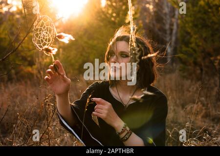 Donna boho con capelli ventosi corti. Silhouette femminile con catcher da sogno attraverso i raggi del sole Foto Stock