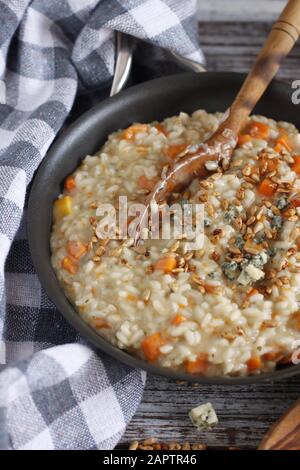 Risotto alla zucca con formaggio blu e semi di girasole con cucchiaio di legno, su sfondo rustico con asciugamano a scacchi blu e bianco Foto Stock