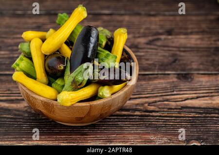 Baby Eggplant e zucchine in ciotola di bambù su sfondo di tavolo di legno Foto Stock