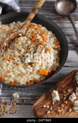 Risotto alla zucca con formaggio blu e semi di girasole, su sfondo rustico con tavola, formaggio e laddle Foto Stock