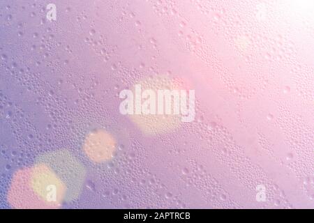 Struttura di fondo in vetro rosa bagnato con gocce di sole e riflessi lenti. Rugiada in condensa Foto Stock