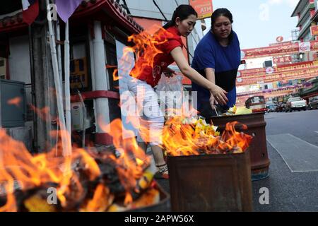 Le donne bruciano oro di carta e denaro finto durante la celebrazione a Chinatown, Bangkok. Il nuovo anno lunare, conosciuto anche come Festival di primavera in Cina, segna l'inizio dell'anno del Rat. La famiglia etnica cinese-tailandese pregano per la buona fortuna e indossano maschere per la protezione dalle polveri mentre il paese lotta per contenere il peggioramento dell'inquinamento atmosferico. Foto Stock