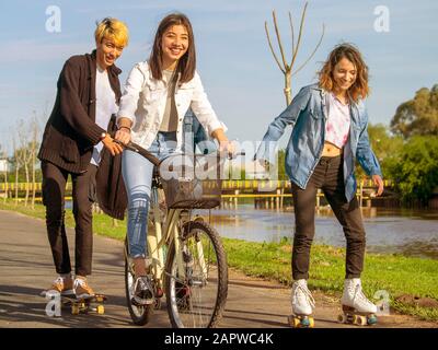 Ragazzi divertirsi all'aperto, accanto a un fiume, con pattini a rotelle e una bicicletta Foto Stock