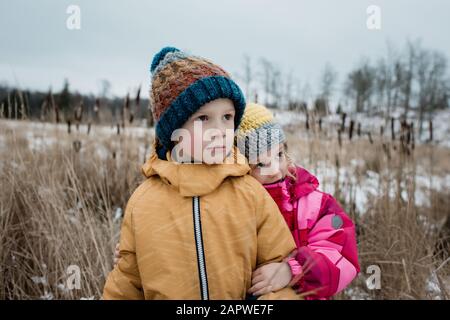 i fratelli si coccolano guardando serio mentre giocano fuori nella neve Foto Stock