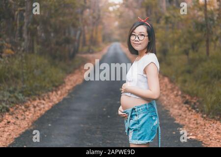 Giovane donna asiatica incinta che indossa abiti e occhiali carini Foto Stock