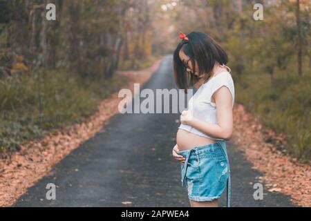 Giovane donna incinta dell'Asia orientale che si aggrapita felicemente Foto Stock