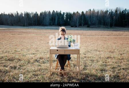 donna flessibile che lavora su una scrivania e un notebook all'esterno in un campo Foto Stock