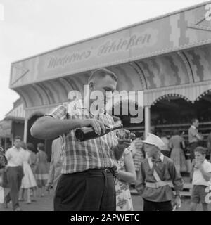 Mosella: Costume e vino Festival Man versa un bicchiere di vino di fronte alla galleria di tiro al terreno fieristico di Rummelplatz Data: 4 luglio 1959 posizione: Germania, Kröv, Renania-Palatinato, Germania occidentale Parole Chiave: Attrazioni della fiera, fiera, pubblico, feste popolari, vino Foto Stock