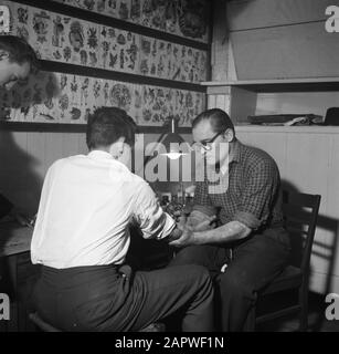 Visita ad un negozio di tatuaggi a Copenhagen l'uomo è tatuato dal tatuatore Jack mentre un uomo è rimasto a guardare Data: Marzo 1954 luogo: Danimarca, Copenaghen, Nyhavn Parole Chiave: Apparecchiature elettriche, edifici, strumenti, uomini, tatuaggi, disegni, negozi Foto Stock