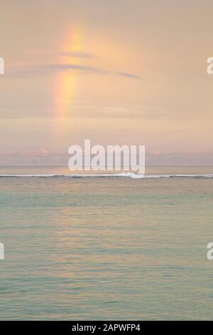 Vista dell'oceano tranquillo con poche onde, con un cielo dai toni chiari e l'arcobaleno Foto Stock