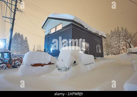 Edifici e automobili sono completamente sepolti in profonda e pesante neve in serata a Yuzawa, Niigata, Giappone. Foto Stock