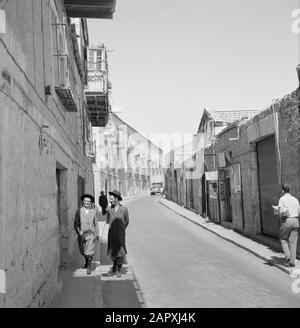 Israele 1964-1965: Gerusalemme (Gerusalemme), Via Mea Shearim nel distretto di Mea Shearim, contenente due giovani che indossano cappotti e cappelli lungo su annotazione: MEA Shearim, anche chiamato Meah Shearim o cento porte, è uno dei quartieri più antichi di Gerusalemme. Fu costruito a partire dal 1870 da ebrei asiatici che vivevano nella Città Vecchia fino ad allora. Tuttavia, c'era troppo poco spazio e così comprarono un pezzo di terra a nord-ovest della città. Questa terra, un'area paludata, fu coltivata in terra per costruire un nuovo quartiere: Meah Shearim. Il distretto è conosciuto anno 2012 come la J ortodossa più estrema Foto Stock