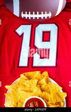 Un calcio americano con chip nacho organici e salsa delicata su una maglia da calcio bianca rossa con il numero 19 Foto Stock