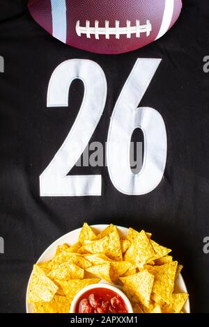 Un calcio americano con chip nacho organici e salsa delicata su una maglia bianca nera da calcio con il numero 26 sulla vista verticale Foto Stock