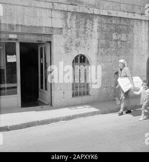 Israele 1964-1965: Gerusalemme (Gerusalemme), Mea Shearim Donna con due figli a portata di mano e pacchetto sotto il suo braccio stretto camminare attraverso la strada Annotazione: MEA Shearim, chiamato anche Meah Shearim o un centinaio di porte, è uno dei quartieri più antichi di Gerusalemme. Fu costruito a partire dal 1870 da ebrei asiatici che vivevano nella Città Vecchia fino ad allora. Tuttavia, c'era troppo poco spazio e così comprarono un pezzo di terra a nord-ovest della città. Questa terra, un'area paludata, fu coltivata in terra per costruire un nuovo quartiere: Meah Shearim. Il distretto è conosciuto anno 2012 come il più estremo ebreo ortodosso Foto Stock