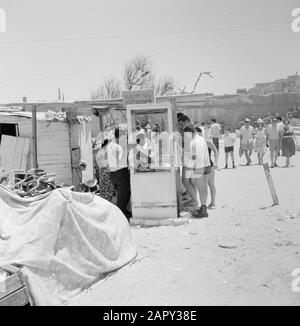 Israele 1964-1965: Tel Aviv, durante il Sabbath al mare la gente vestito Summerly compra il cibo sul bordo della spiaggia in una stalla costituita da porte e partizioni di legno Annotation: Durante il Sabbath attira molte persone da Tel Aviv al mare Date: 1964 Location: Israel, Tel Aviv Keywords: bagnanti, vita quotidiana, biciclette, paratie, spiagge, alimenti Foto Stock