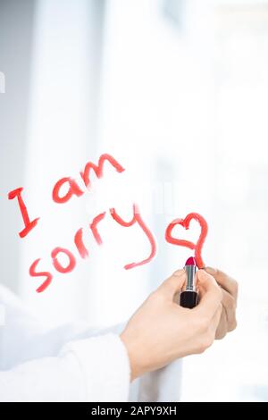 Mano di giovane donna scritta messaggio sullo specchio con rossetto di colore cremisi Foto Stock