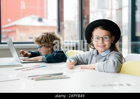 Cute diligente scolaretta in casualwear e occhiali facendo note Foto Stock