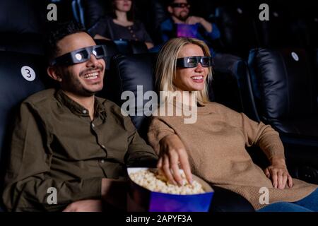 Felice giovane coppia in occhiali 3d mangiare popcorn mentre godendo il tempo in cinema Foto Stock