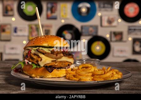 Hamburger vegan fatto in casa con ceci, funghi saltati, formaggio Emmenthal e patatine fritte su tavola di legno. Immagine isolata. Foto Stock