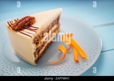 Pezzo di torta di cioccolato e crema di latte, le carote e i dadi isolato su una piastra di colore blu Foto Stock