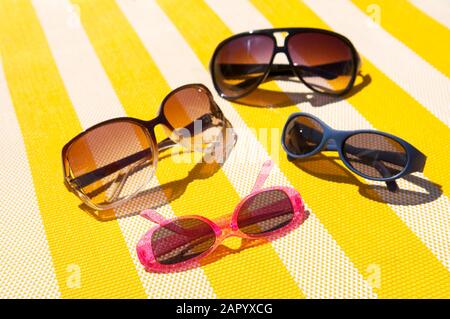 Famiglia di occhiali da sole seduti al sole su sfondo giallo brillante e bianco a strisce sulla sedia da spiaggia Foto Stock