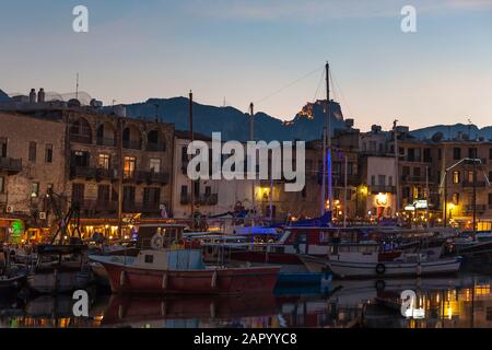 Serata sul porto di Kyrenia (conosciuto anche come Girne), nella parte settentrionale di Cipro, con il Castello di S. Hilarion illuminato sulla montagna oltre Foto Stock
