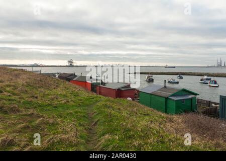 Una vista da Paddys Hole, Redcar, Inghilterra, Regno Unito, che mostra le capanne dei pescatori, barche ormeggiate e sfondo industriale Foto Stock