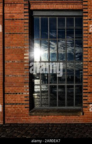 Finestra in muratura con riflessione del porto container di Amburgo e nuvole e sunstar nel cielo Foto Stock