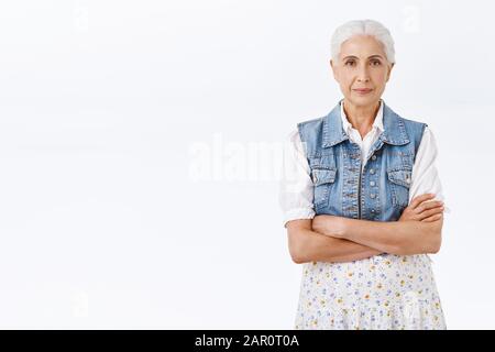Donna anziana con capelli grigi pettinati, indossando elegante giubbotto denim su vestito, croce petto mani con impaziente, espressione irritata fotocamera look Foto Stock