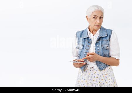 La donna anziana, confusa e interrogata, non riesce a capire di cosa si trattava la telefonata, mette in attesa lo smartphone, punta al dispositivo mobile, stare fotocamera perplesso e. Foto Stock