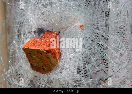 finestra con tende a rete schiacciata con mattoni rossi di vecchio stile in un atto di vandalismo odio danno criminale Foto Stock